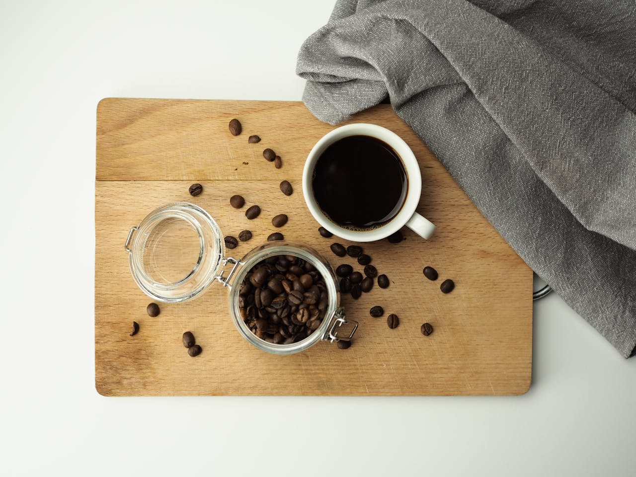Flat lay image of a coffee cup, beans, and glass jar on a wooden board with a napkin. Perfect for coffee-related themes.